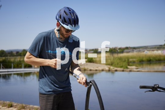 Ein Radfahrer pumpt mit einer kleinen Luftpumpe Luft einen Fahrradschlauch.