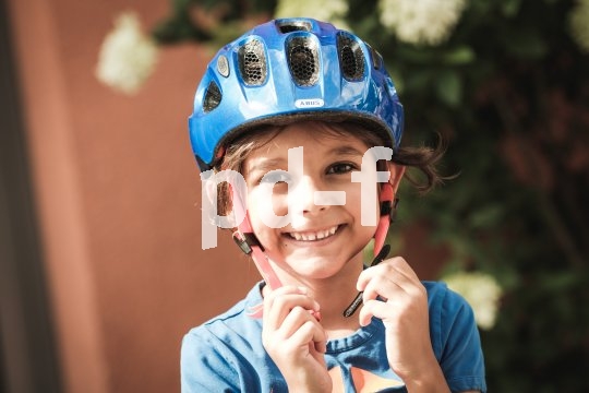 Ein lachendes Kind mit den Händen am offenen Kinnriemen eines blauen Fahrradhelmes.