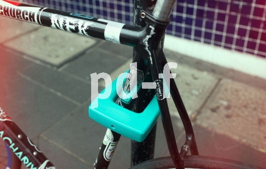 Ein türkisfarbenes Bügelschloss sichert ein Fahrrad an einem Metallpfosten.