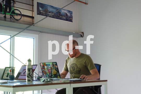 Ein Mann sitzt an einem Schreibtisch vor einem Laptop, der mit vielen Aufklebern verziert ist.