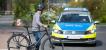 Eine Person schiebt ein Fahrrad über einen Fußgängerüberweg und schaut zu einem Polizeiauto auf der Fahrbahn.