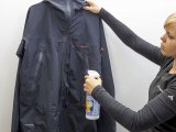 Eine Frau besprüht eine Jacke mit Imprägnierung aus einer Pumpsprühflasche.