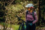 Frau mit Helm schiebt Mountainbike durch Wald