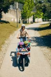 Frau fährt mit Cargobike und Kindern durch Park.