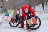 Weihnachtsmann fährt mit Rad durch Wald und hat Geschenke dabei.