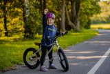 Ein Kind steht mit einem Fahrrad am Straßenrand und streckt jubelnd eine Faust in die Höhe.
