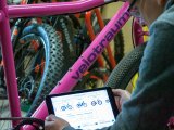 Eine Person hält ein Tablet vor den Rahmen eines Fahrrades. Auf dem Display sind kleine Abbildungen von Fahrrädern zu sehen.