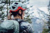 Frau mit Mountainbike-Helm und Rucksack blickt auf Berg.