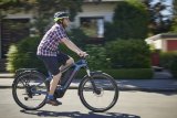 Ein lächelnder Mann fährt auf einem E-Bike durch ein Wohngebiet.
