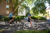 Ein Mann und ein Kind fahren auf Fahrrädern eine Straße zwischen Wohnhäusern entlang.