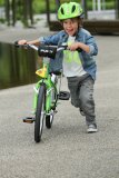Ein Kind mit grünem Helm schiebt ein grünes Fahrrad.