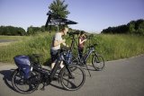 Zwei Personen stehen vor einem Schild des Nationalparks Harz und schauen in Fernrohre auf Stativen. Neben ihnen stehen E-Bikes.