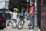 Ein Mädchen und eine Frau stehen mit Fahrrädern auf einem Bürgersteig. Beide tragen Helm.