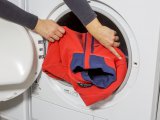 Eine Person steckt eine Jacke in eine Waschmaschine.