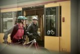 Zwei Personen schieben Mountainbikes vor der offenen Tür einer Bahn entlang.