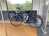 Ein blaues Fahrrad lehnt in einem Zug an Klappsitzen. Am Lenker hängt ein Helm.