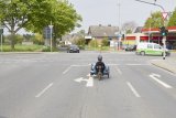 Eine Person auf einem Liegedreirad fährt auf einer Abbiegespur auf eine Straßenkreuzung.