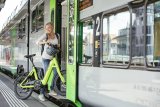 Eine Frei steigt mit einem E-Bike mit kleinen Rädern in einen Zug ein.